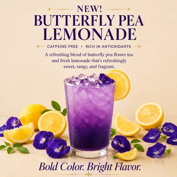 A glass of purple butterfly pea lemonade with ice, lemon slices, and butterfly pea flowers.