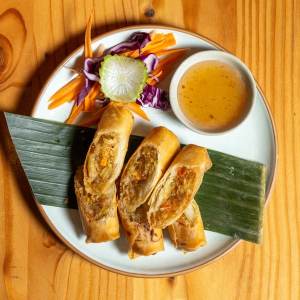 Crispy spring rolls, cut in half, with a side of sweet chili sauce and fresh salad.