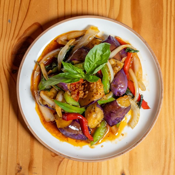 Stir-fried eggplant with onions, bell peppers, and basil in a savory sauce on a white plate.