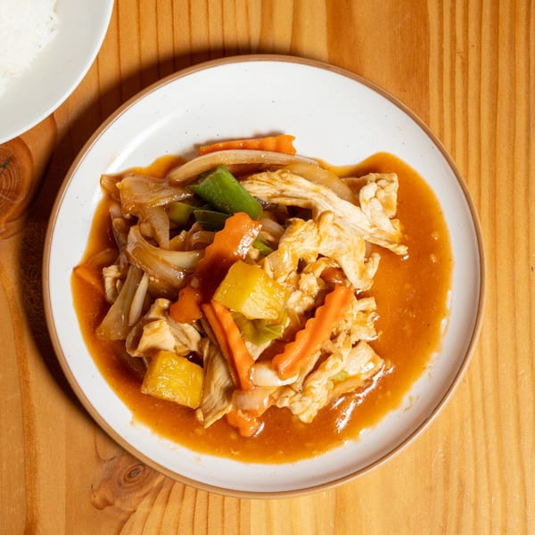 Sweet and sour chicken with pineapple, carrots, and onions on a white plate.