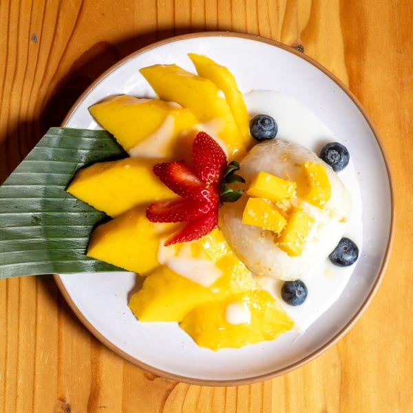 Mango sticky rice dessert with blueberries and a strawberry on a white plate with banana leaf.